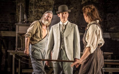 Akie Kotabe wears a grey suit and bowler hat. He stands between David Threlfall and Ruth Wilson. David and Ruth wear shirts and dungarees and Akie looks at Ruth.