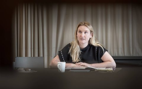 Lizzie Manwaring wears a black top and sits at a table with her arms crossed.