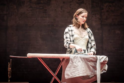 Look Back in Anger Production Photo Morfydd Clark stood behind an ironing board, ironing a shirt.