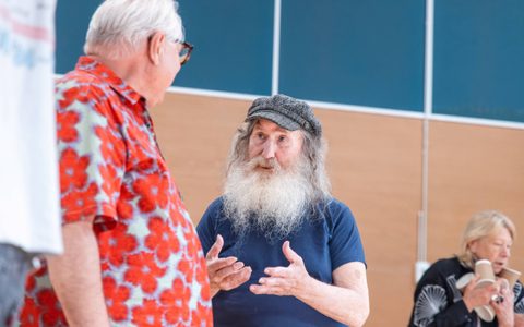 Two people speak to each other in a rehearsal room.