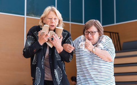 Two people link arms, with one holding coffee cups.