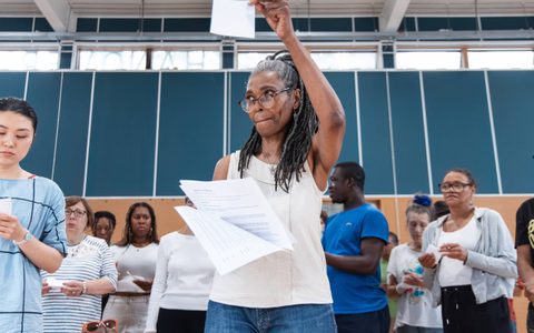 A person raises their arm and holds a script in a rehearsal room.