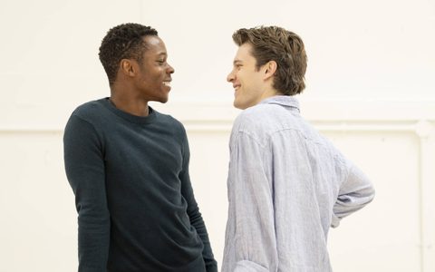 Alistair Nwachukwu wears a dark teal top and faces Jasper Talbot, who wears a blue shirt. They smile at each other.