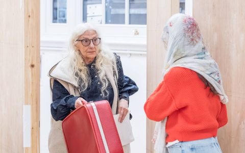 Souad Faress stands holding a red and white suitcase in rehearsals for Under the Shadow.