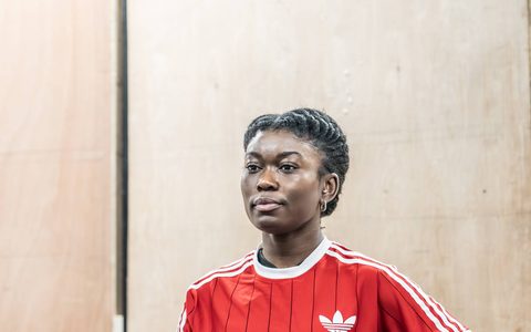 Tanisha Spring wears a red top and stands with both hands on one hip, looking straight ahead.