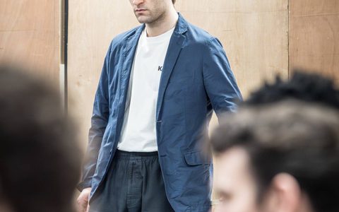 Arty Froushan wears a white top under a blue blazer. He looks darkly towards something off camera.