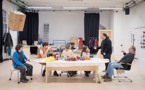 The Christmas Day company sits around a table in a rehearsal room. They look at Jamie Ankrah, who is standing and speaking.