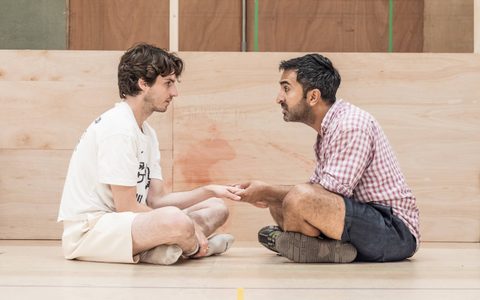 Luke Cinque-White and Parth Thakerar sit cross legged on a floor holding hands.