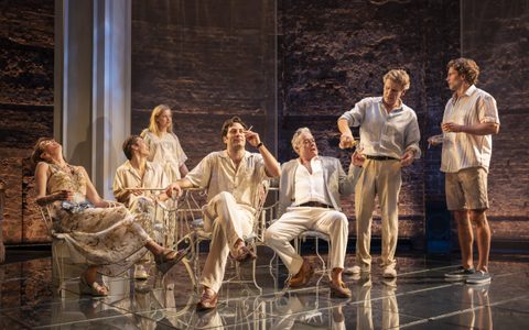 The Line of Beauty company sit at a table on stage.