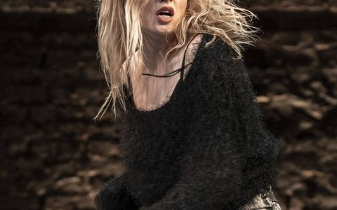 Ellie Bamber wears light wash jeans and a black fuzzy top. She is mid-motion and looks distraught.