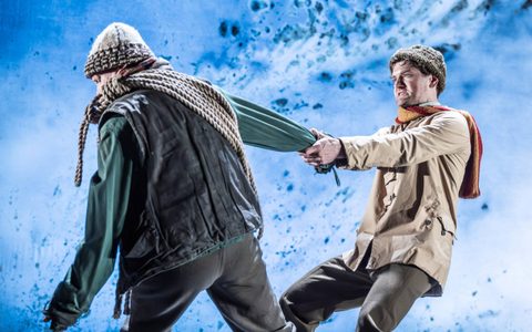 Kyle Soller wears a woolly hat and scarf and leans back, pulling on Jerry Killick’s arm, who leans away from him. Jerry has a long rope wrapped over his shoulder. The background is an icy cold blue.