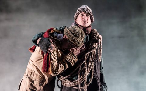 Jerry Killick wears a woolly hat and scarf. He has a long rope wrapped over his shoulder, and holds Kyle Soller to his chest with one arm, who also wears a woolly hat.