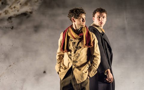 Kyle Soller wears a dark beige jacket and a yellow and red scarf. He looks off to the side with his hands in his pockets. Stuart Thompson stands behind him, wearing a dark coat and looking to the side.