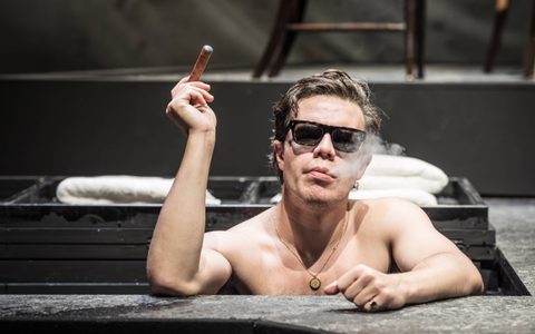 Oliver Johnstone rests on the edge of an ice bath, wearing black sunglasses and smoking a cigar.