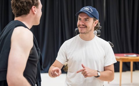 Oliver Johnstone wears a white t-shirt and a blue cap. He gestures with his hands and smiles as he speaks to Stuart Thompson, who faces away from the camera.