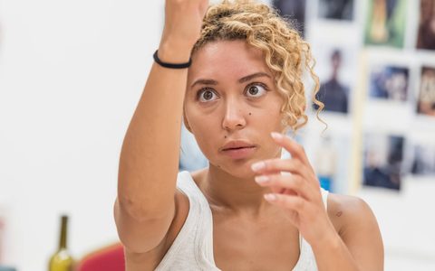 Yanexi Enriquez wears a white tank top and holds her hands up in front of her, gazing forward with an intense, wide-eyed expression.
