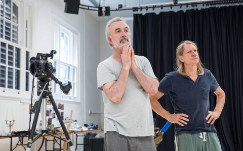 Declan Conlon wears a light t-shirt and stands near a camera, with his hands together at his chin. Jerry Killick stands near him, wearing a blue t-shirt and with his hands on his hips.