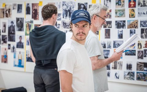 Oliver Johnstone wears a white t-shirt and blue cap. He looks off to the side. Declan Conlon and Stuart Thompson stand in the background.