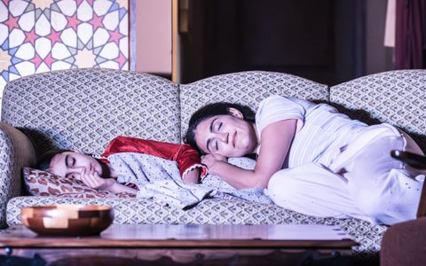 Esma Akar and Leila Farzad lie on a sofa with their eyes closed.