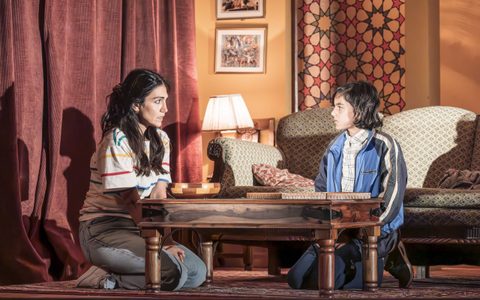 Leila Farzad and Jago Agrawal kneel at a wooden coffee table in a living room.