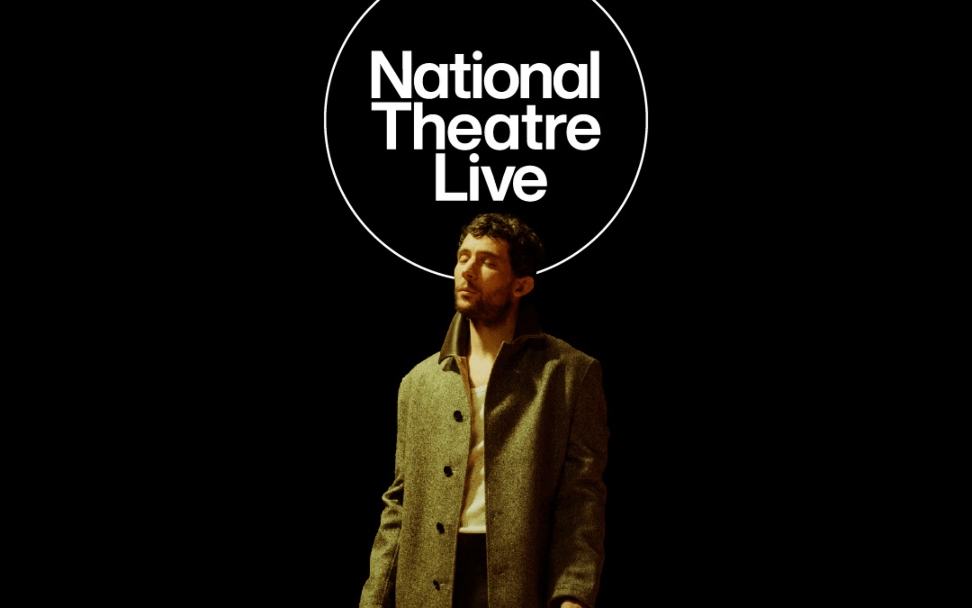 Josh O' Connor stands under an amber light with the words National Theatre Live above his head.