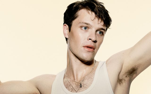 Jasper Talbot is dancing with his arms held up whilst wearing a white vest. 