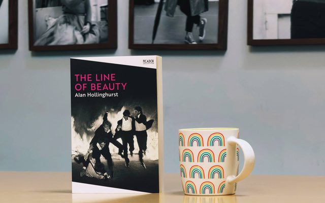 The Line of Beauty book next to a rainbow-patterned mug.