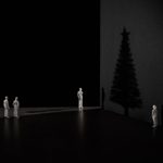 The shadow of a Christmas tree against a dark wall, with four small white figurines looking at it. 