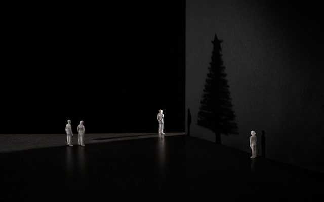 The shadow of a Christmas tree against a dark wall, with four small white figurines looking at it. 