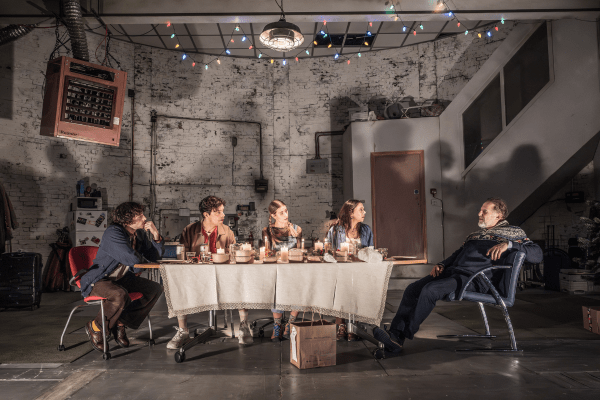Production photo of Christmas Day: The family sit around the table talking, with a takeaway in front of them.