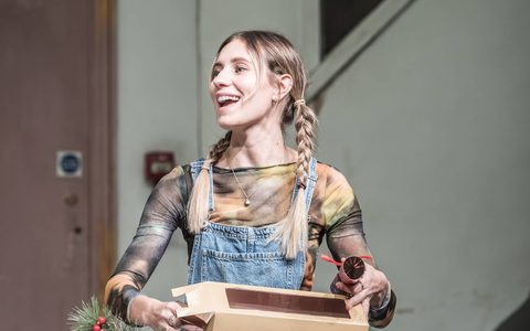 Callie Cooke smiles off to the side, unpacking crackers from a cardboard box on a dining table. She wears blue dungarees.