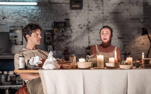 Bel Powley sits next to Jacob Fortune-Lloyd at a dining table laden with food containers. She cries, and Jacob leans back, looking at her.