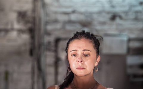 Bel Powley wears a white vest and sits at a dining table. She is crying.