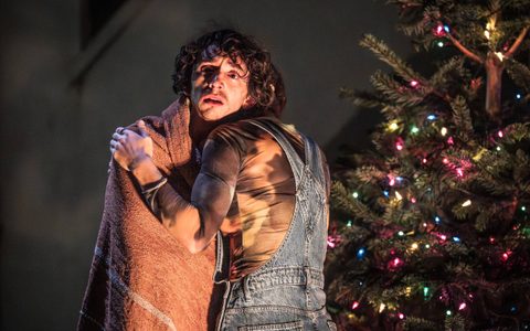 Callie Cooke holds Samuel Blenkin, who has a blanket wrapped around his shoulders. The stage is dark and there is a Christmas tree near them.