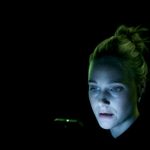 Romola Garai looks at a phone against a black background