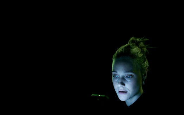 Romola Garai looks at a phone against a black background
