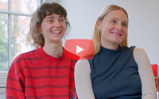 Tanya Reynolds and Romola Garai smile. Red play button mid-screen.