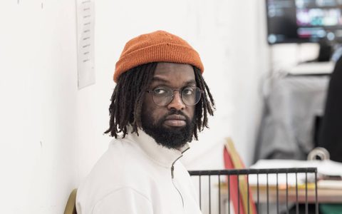 Assistant Director Phillippe Cato wears an orange hat, glasses and a white long-sleeved top.