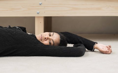 Thalissa Teixeira lies on the floor under a wooden bench with one arm stretched out.