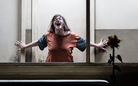 Pearl Chanda can be seen through a large window. She presses her hands on the wall behind her and she screams with her eyes closed.