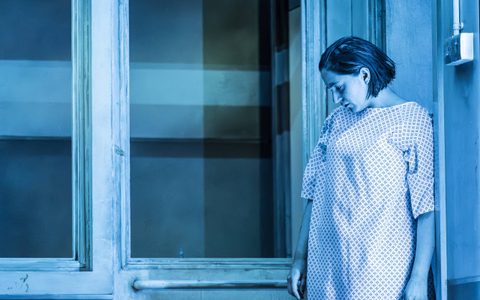 Pearl Chanda stands in a hospital gown looking down at the floor.