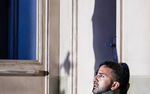 Parth Thakerar sits leaning against a wall. The tall shadow of Leo Bill can be seen against the same wall.