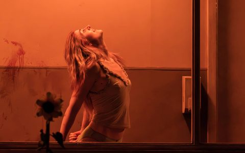Lizzy Connolly stands behind a large window, her back is arched, her head is tipped back and she looks towards the ceiling.