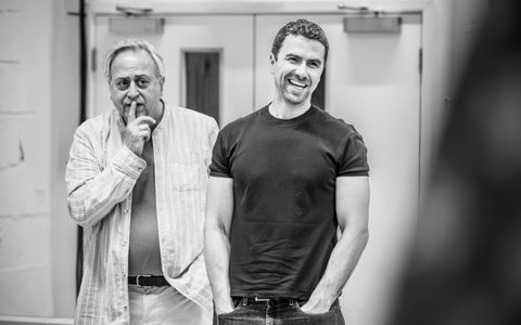 Richard Fleeshman stands laughing, he wears a black top and jeans and has his hands in his pockets. Next to him is Stanley Townsend, who has one finger rested against his lips.