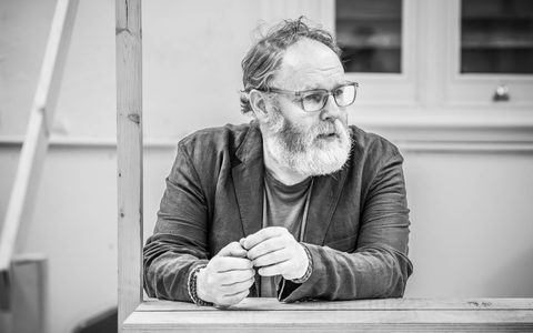 David Ganly leans against a surface with his hands together. He looks over his left shoulder.