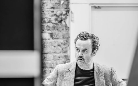 Daniel Mays stands with his hands on his hips. He is looking over to the right with a shocked expression on his face.