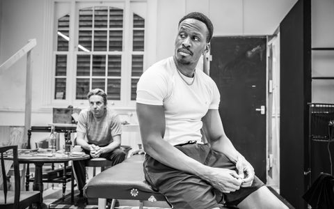 Patrick Martins sits on a massage table with his hands together in front of him. Oliver Ryan sits in the background with his hands clasped.