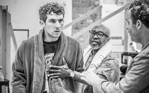 Patrick Martins holds Josh O'Connor, who is wearing a towel robe and an angry expression, back from Daniel Mays.